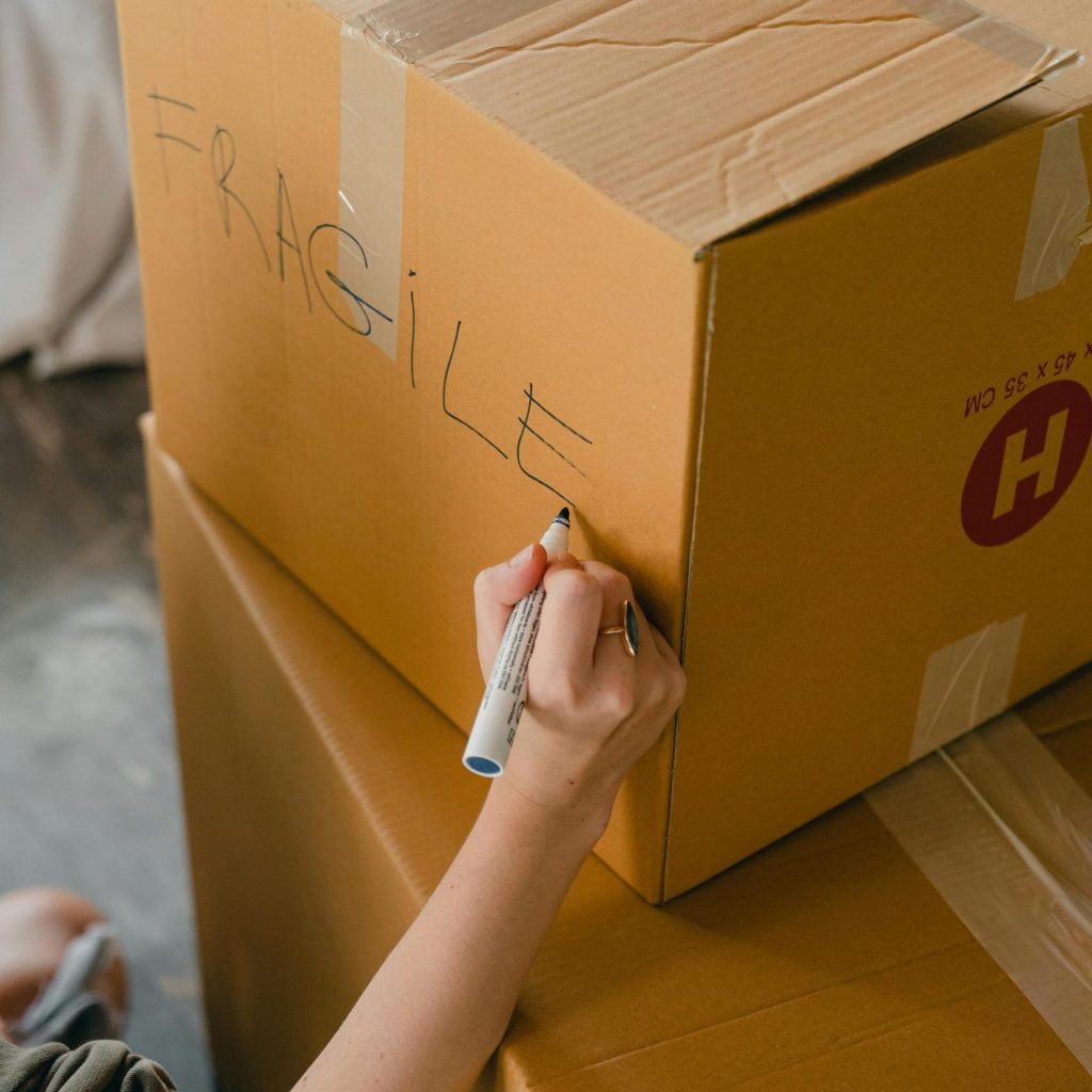 A person writes 'fragile' on a cardboard box using a marker while preparing for a move.